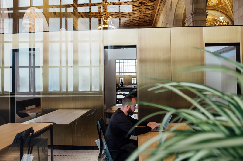 a man working on a laptop in an open office space with a glass wall, working in open office space 4k