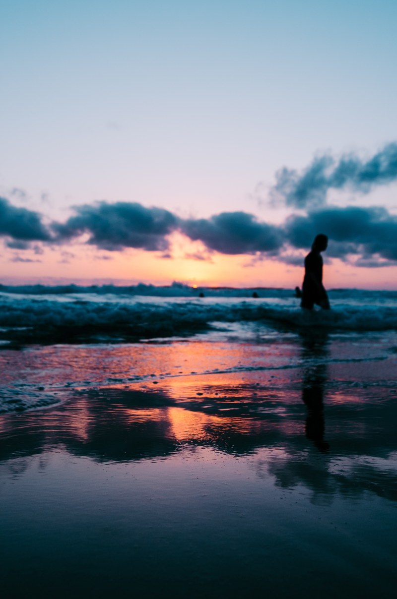 surfer silhouette on the wet sand beach at sunset, shallow sea at sunset 4k