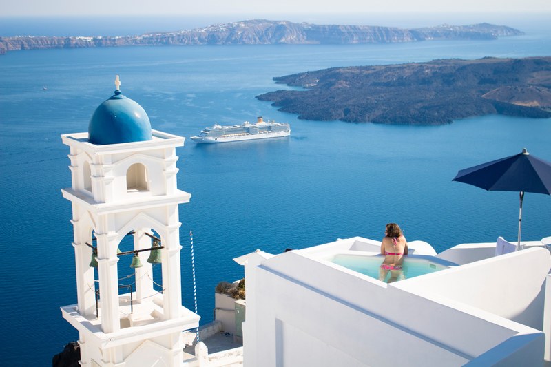 a woman in a swimsuit stands up in a tiny pool at the top of a white building in a classic greek seaside town, woman near a pool 4k