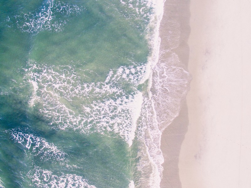 a drone shot of waves crashing on an empty sandy beach, deserted beach in birds eye view 4k
