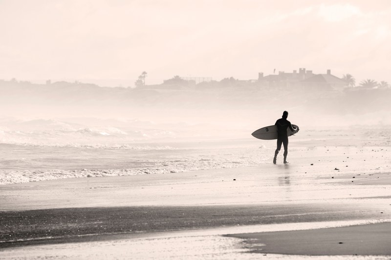 surfer walking on the beach by the rough ocean in cape town, surfer heading into the mist 4k