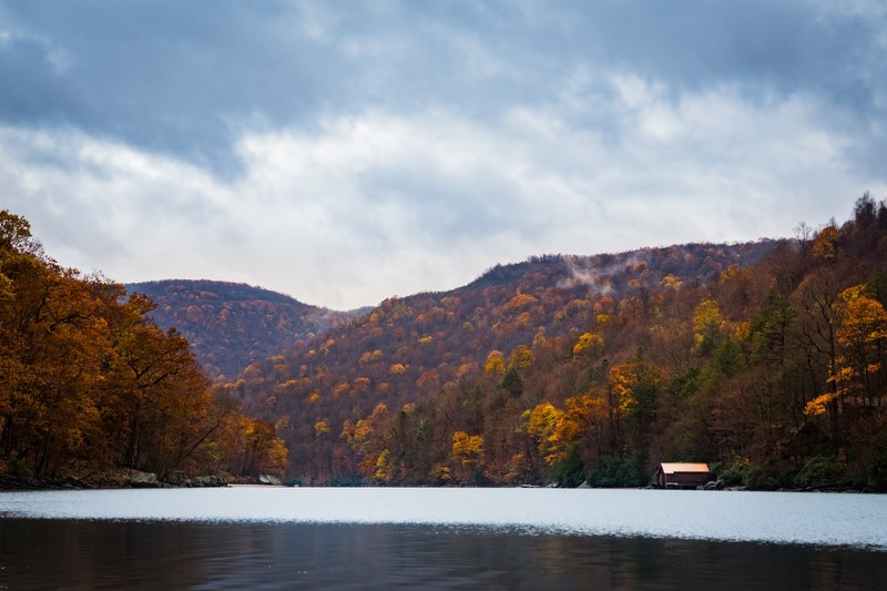 the half frozen cheat lake with a boathouse and orange leaved trees on its shore, cheat lake in the winter 4k