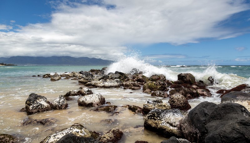 a wave splashing in on large rocks on a beach, _splashing beach rocks 4k