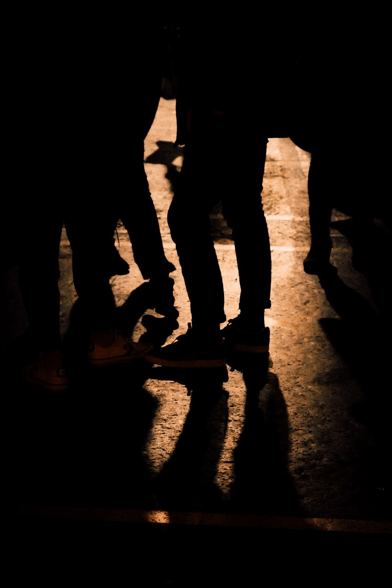 silhouettes of people standing in a dimly lit street seen from the waist down, silhouettes in the street 4k