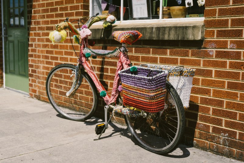 a parked bicycle with colorful crocheted yarn wrapped around its handlebars seat and frame, colorful yarn on bike 4k