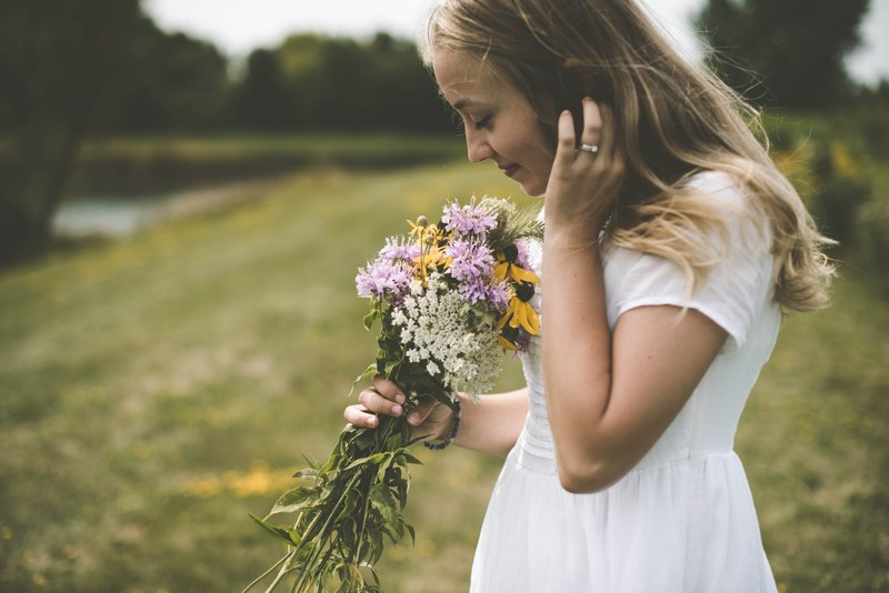 a woman wearing a white dress smelling a bouquet of wildflowers outside in cedar falls, cedar falls flowers 4k