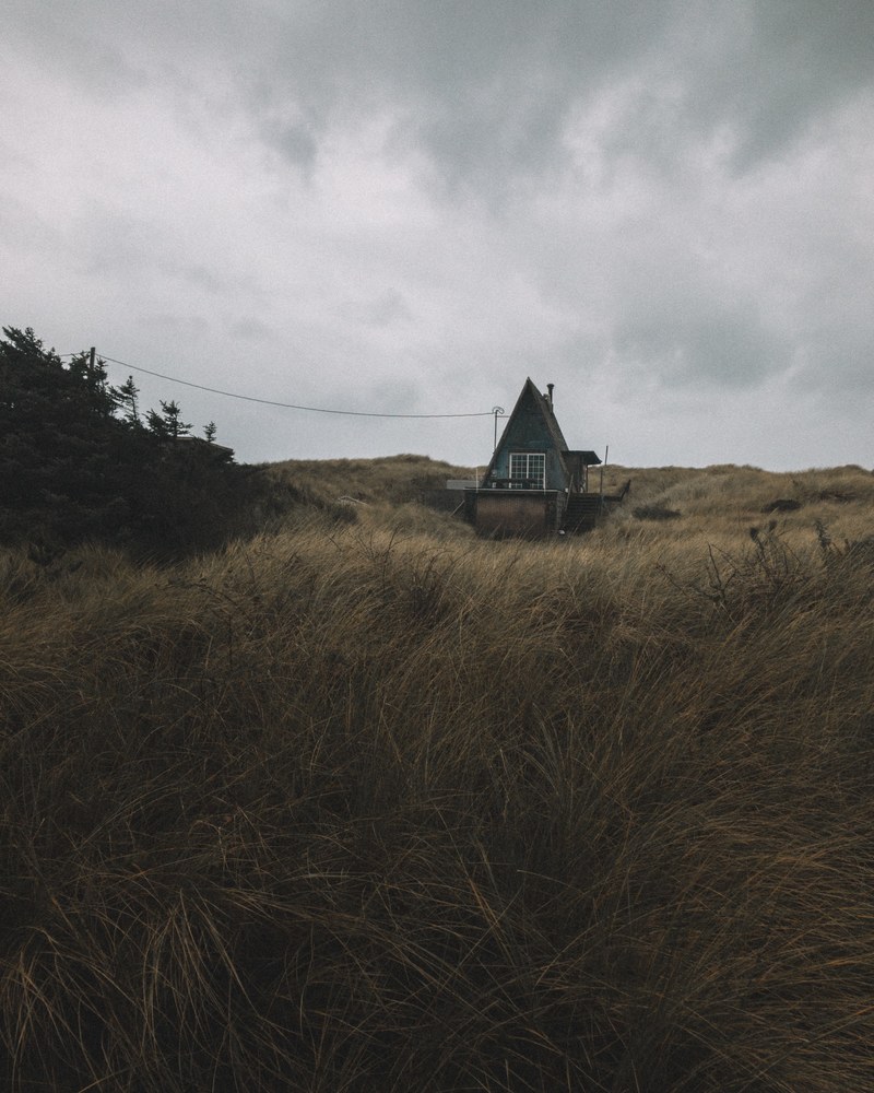 a small hut in a grassy field on a cloudy day, small hut under overcast sky 4k
