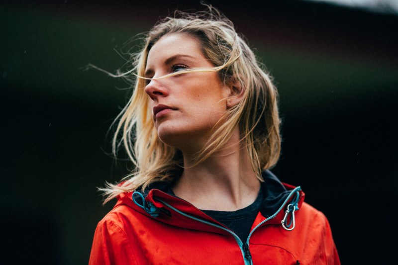 a woman in a red jacket with her hair blowing over her face, may rain 4k