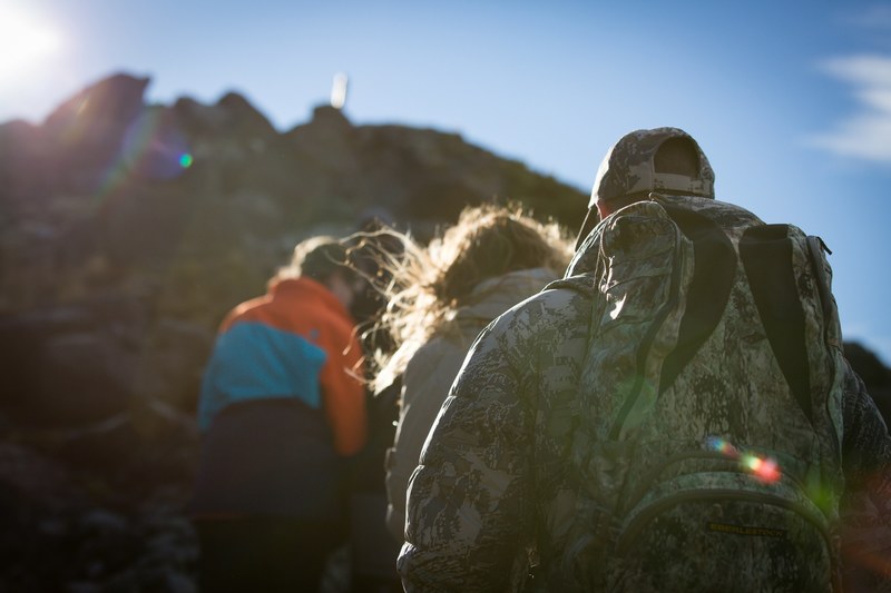 a group of hikers facing away from the camera climb a stone wall on fox glacier, the hike 4k
