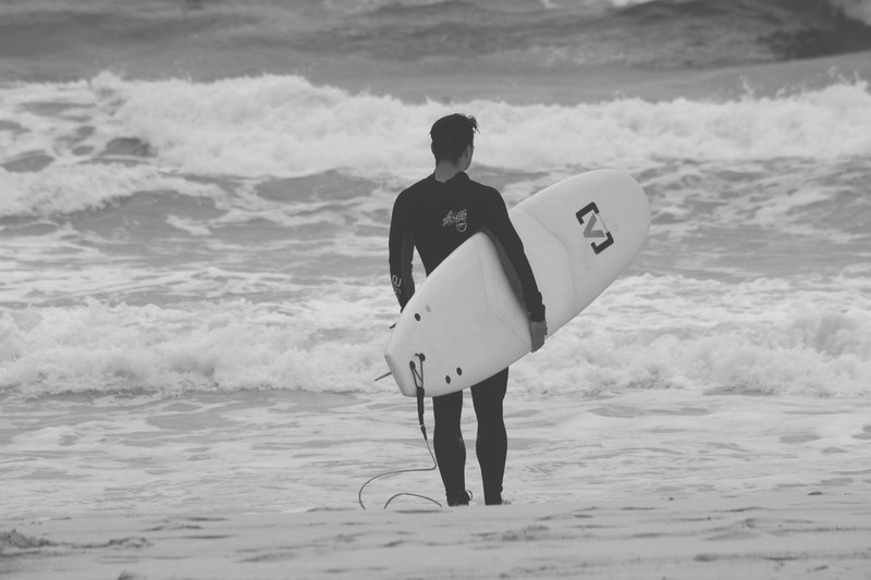 a surfer wearing a wetsuit holding a surfboard looking out into the ocean, black and white surfer 4k