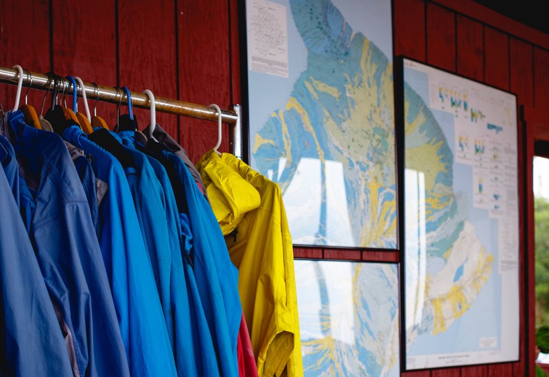 a rack of raincoats next to several framed maps hanging on a red paneled wall, you are here 4k