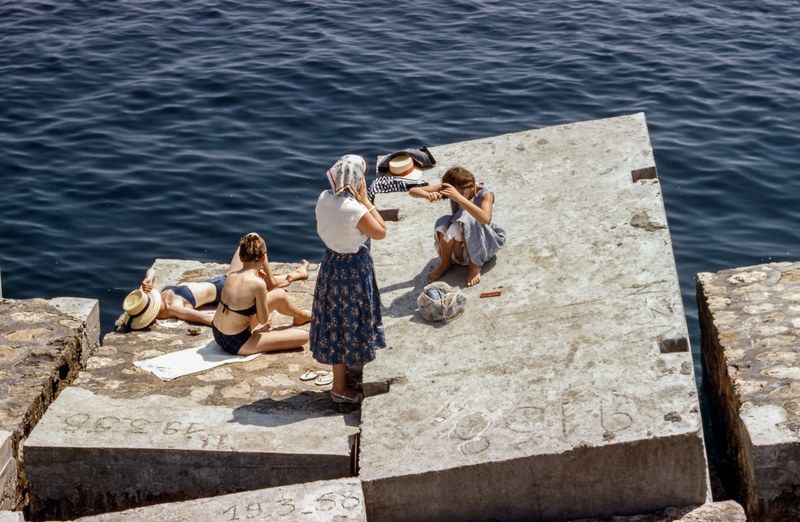 women in swimsuits and vintage clothing sunbathing on cement cubes by the sea, women sunbathing by the sea 4k