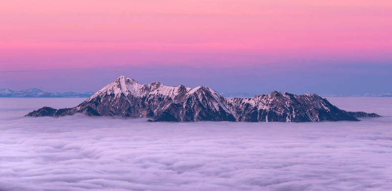 snowcapped mountain peaks above clouds a purple and pink sky in the background, out of the fog 4k