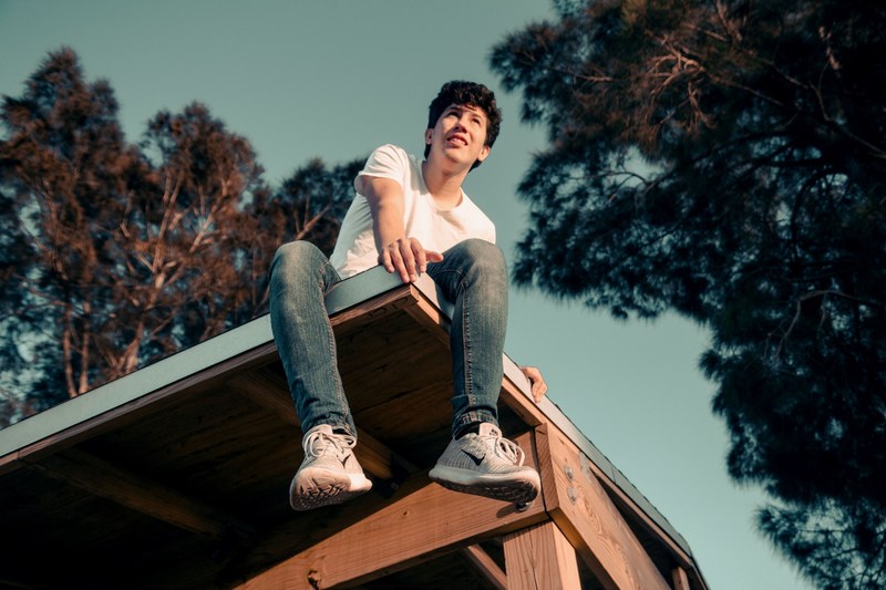 a young man in blue jeans and nike sneakers is sitting on top of a roof, _rooftop views 4k
