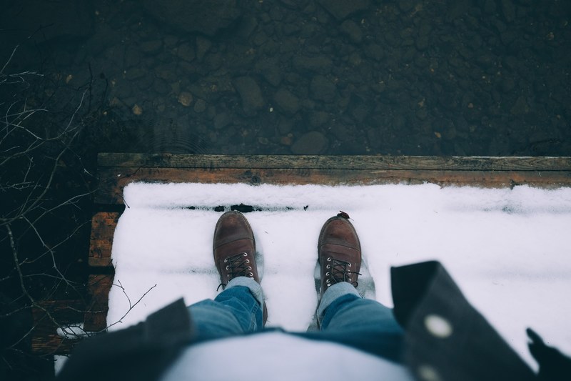 a person looking down at a pair of brown shoes in snow covered dock by the water, _know who you are 4k