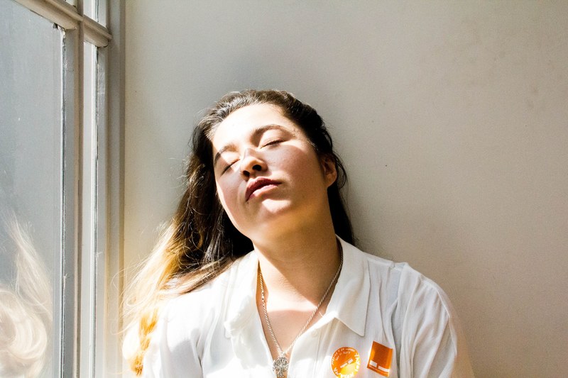 tired woman wearing a uniform closes her eyes near a sunny window, contemporary 4k