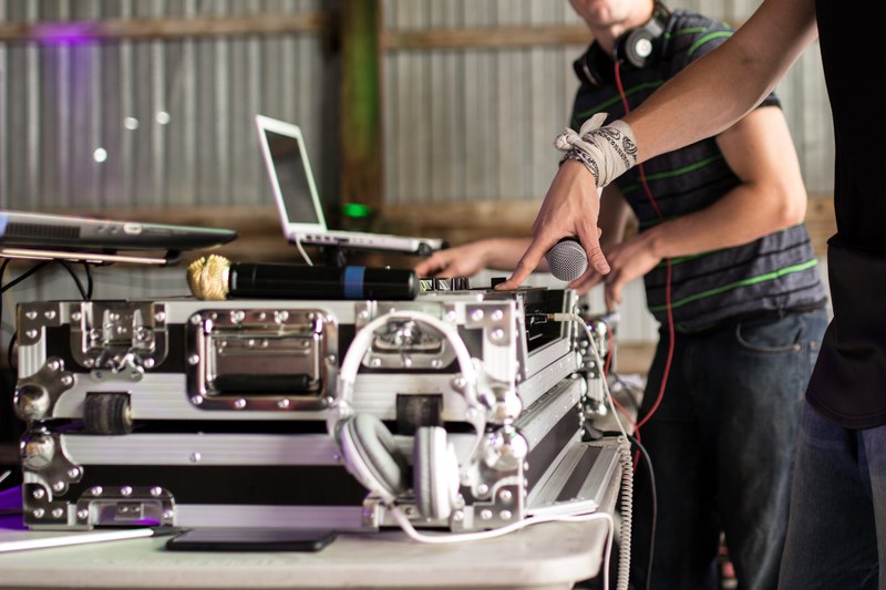 a dj with a bandana wrapped around his wrist mixing on a turntable and mixer beside two laptops a microphone white headphones a smartphone and another dj wearing beats headphones, djs mixin 4k