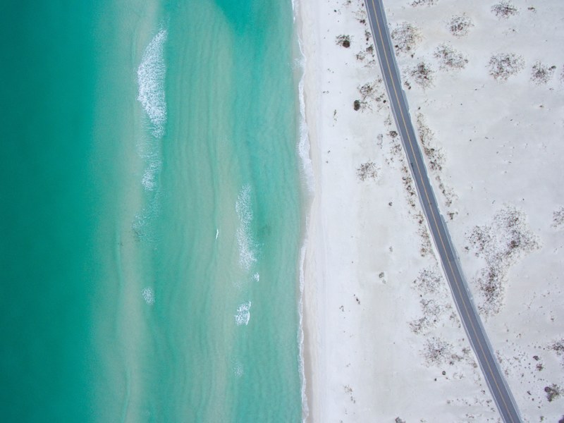 drone aerial view of a road through the white sandy beach by the ocean at gulf breeze florida, _drone view of road on beach 4k