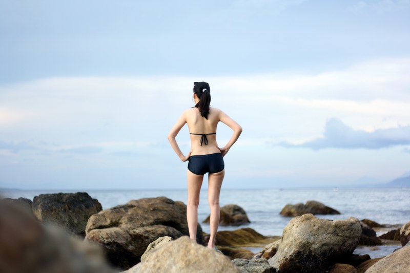 an attractive woman standing on large rocks looking out into the ocean, woman staring in ocean 4k