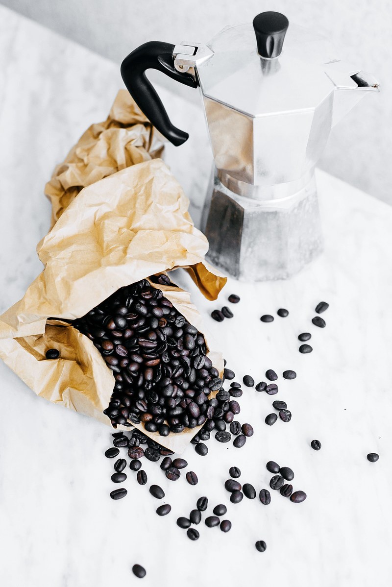 coffee beans in a paper bag spilling onto a counter next to a silver coffee pot, coffee 4k