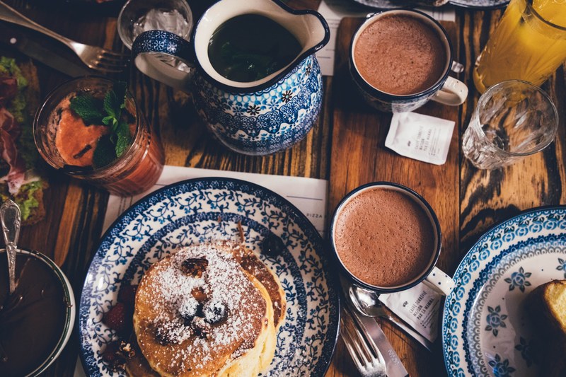 an overhead shot of a breakfast table with pancakes mugs drinks and food, breakfast table with pancakes 4k