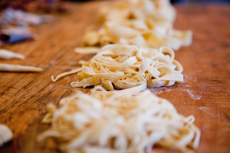 mounds of handmade uncooked pasta noodles lined up on a wooden surface, handmade pasta noodles 4k