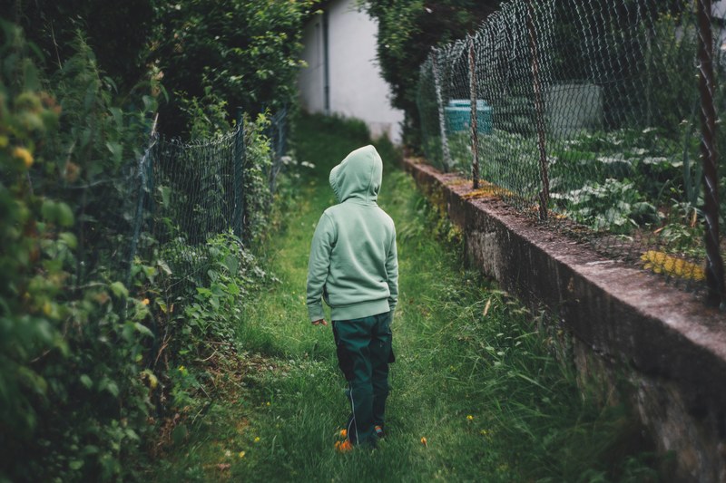 curious child in a hoodie walks alone through a garden, kid in a garden 4k