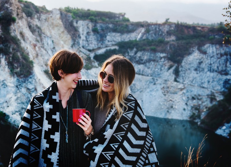 two women stand closely wrapped in a blanket in front of a rocky landscape, woman wrapped in blanket 4k
