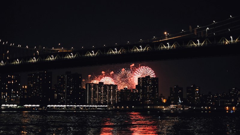 fireworks go off behind the new york city skyline beneath the brooklyn bridge, celebrating 4th of july at nyc 4k