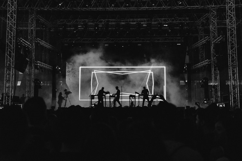 black and white shot of band playing on stage with neon backdrop and crowd in athens, moderat 4k