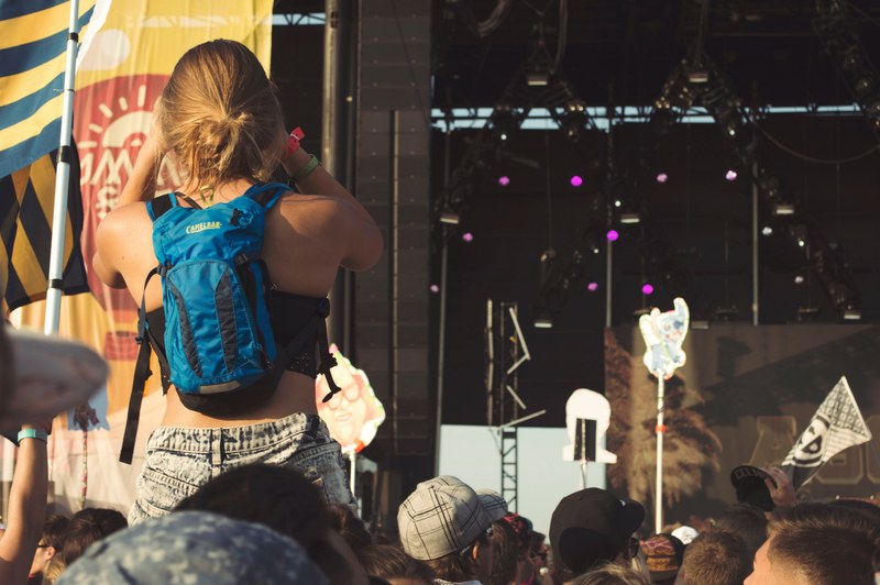 woman sits on a friends shoulders before an outdoor concert at a music festival, festival goers 4k