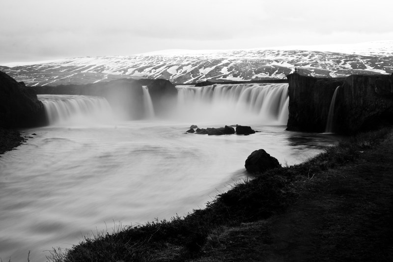 black and white shot of waterfall flowing over rock and grass in foreground, monochrome big waterfall 4k
