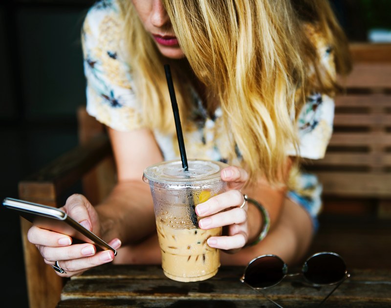 a blonde woman drinking iced coffee while using an iphone, texting over iced coffee 4k