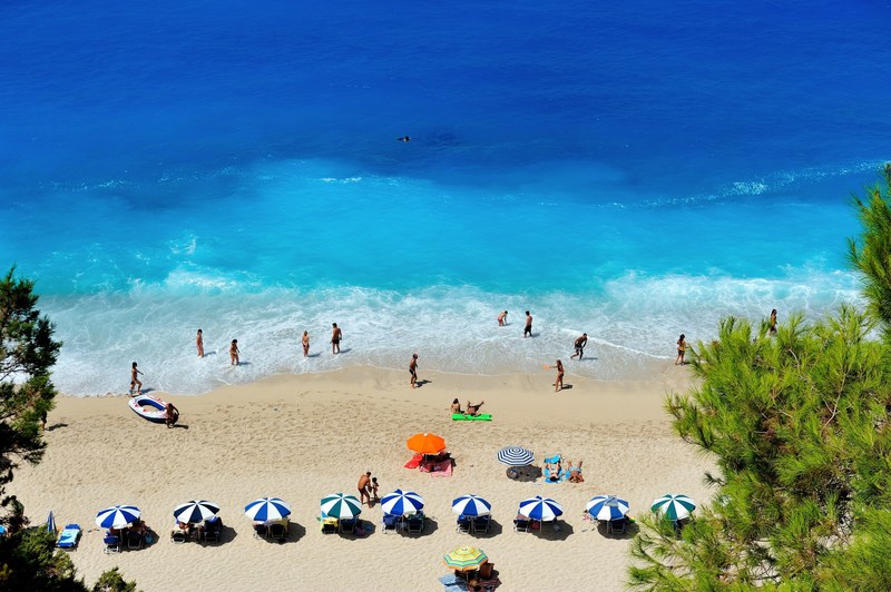 vacationers reclining on deck chairs and wading through the blue water on a small beach, golden beach during summertime 4k