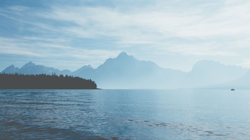 view from a lake on the silhouettes of tall mountains behind fog in grand teton national park, mountain lake in grand teton national park 4k
