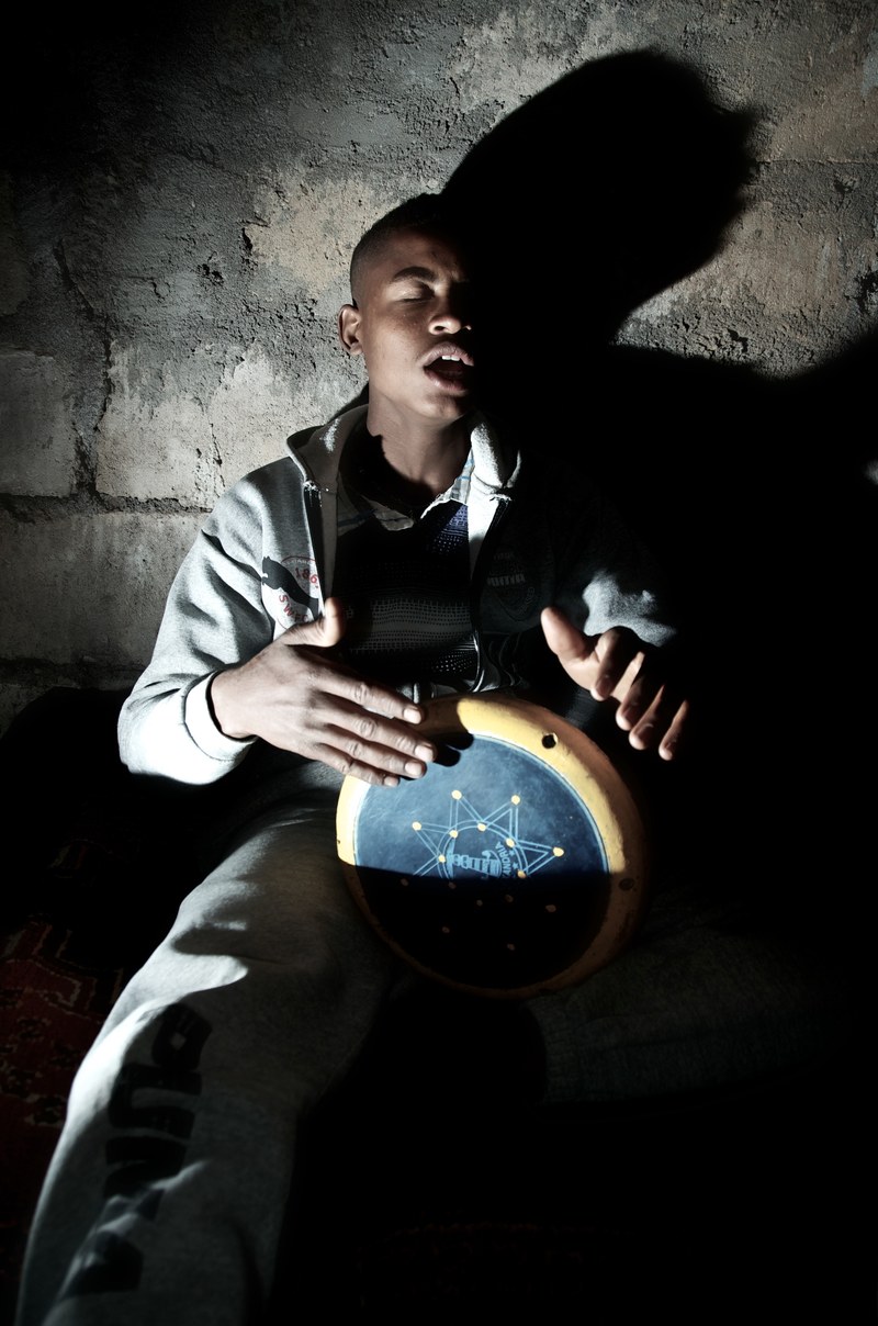 a man seated against a bare brick wall and playing a drum, expressive drum player 4k