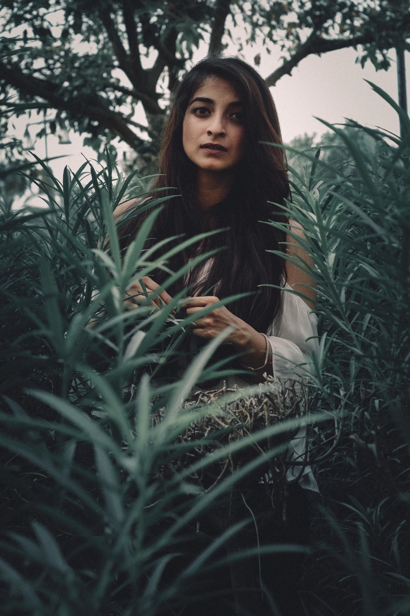 woman with long hair standing among luch green plants, hidden in the ferns 4k