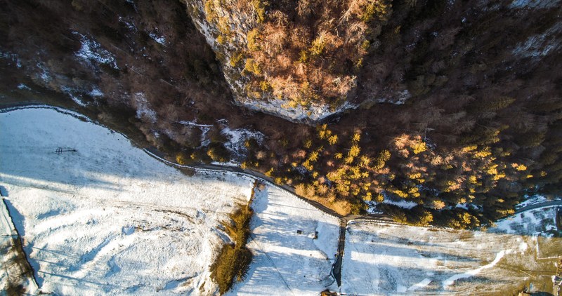 a drone shot of a road between a coniferous forest and snowy fields, the cliff 4k