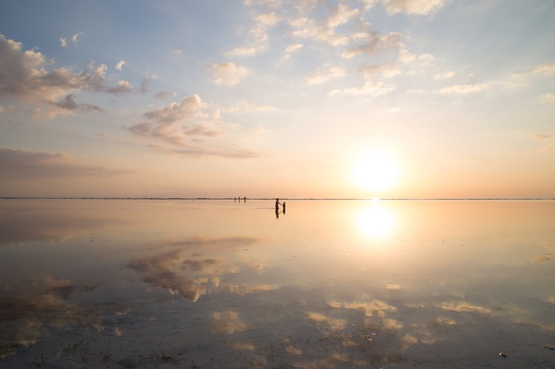 in the distance silhouettes of figures playing in the water which reflects the sky and setting sun, mirror reflection of sunset 4k