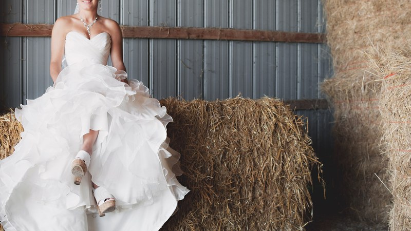 happy bride in a wedding gown sits atop bales of hay in a barn, bride in hay barn london 4k