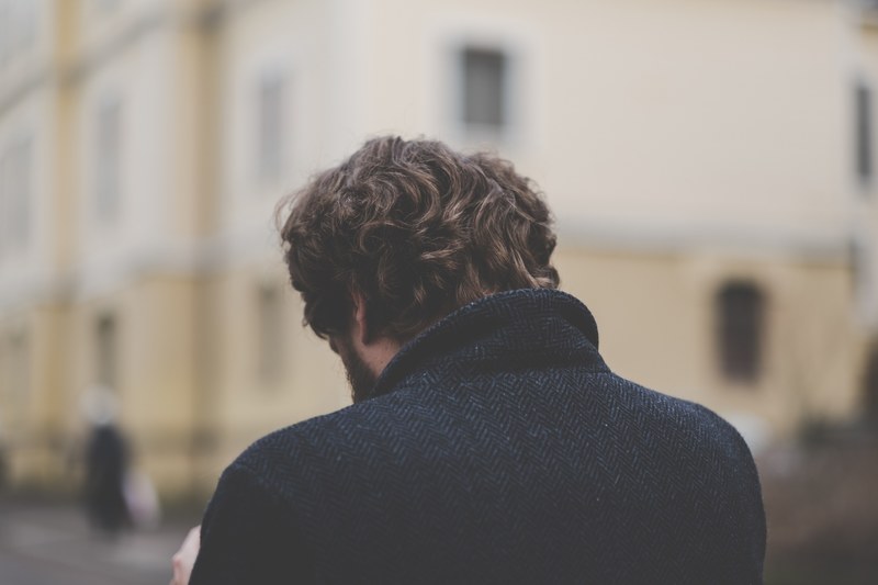 the back of a man with his head bowed thinking outdoors in a city, man thinking with bowed head 4k
