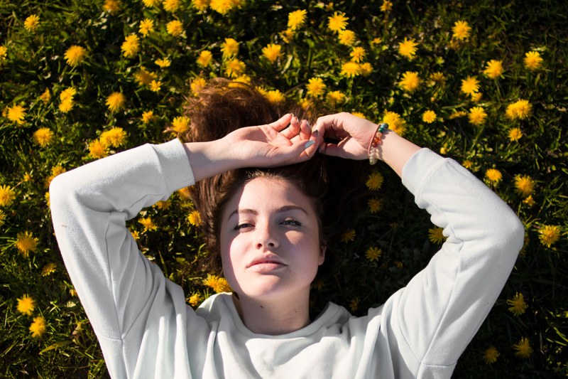 a woman in a sweatshirt lays in a field of yellow dandelions, woman in field of dandelions 4k