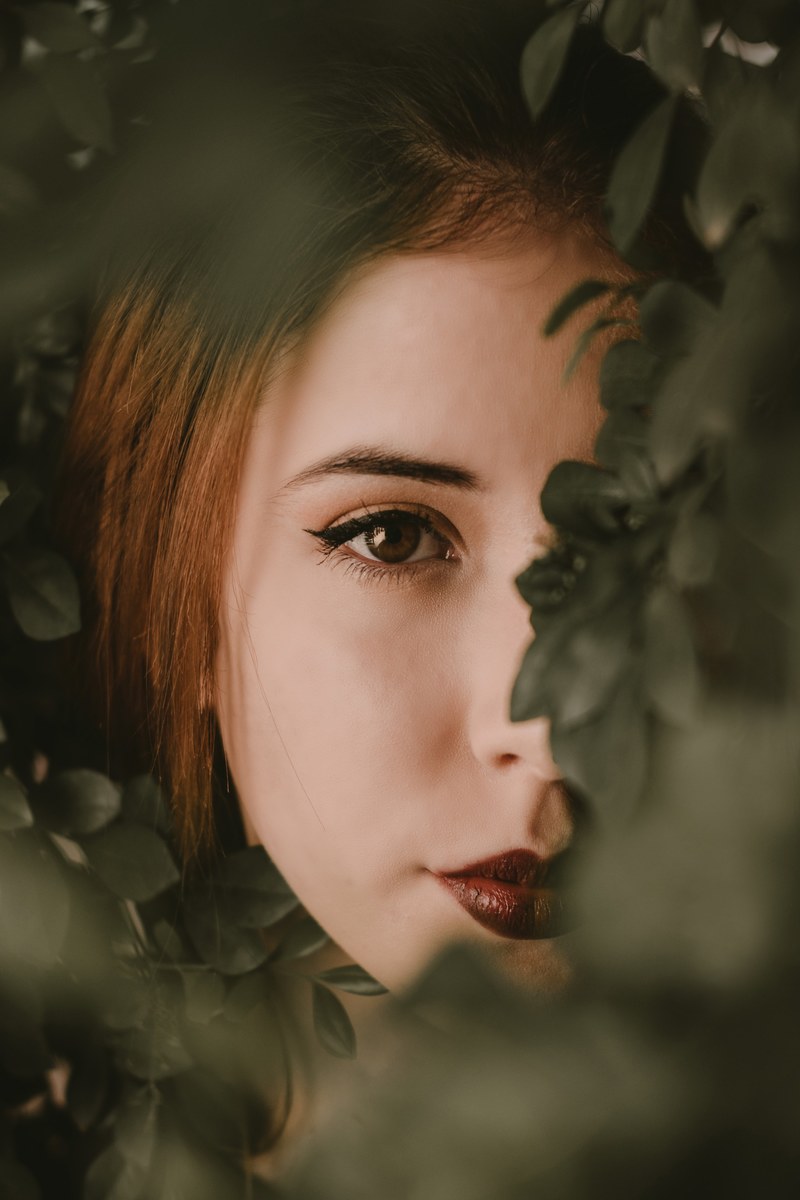 woman with bold lips and winged eyeliner hiding behind leaves, lost in her eyes 4k