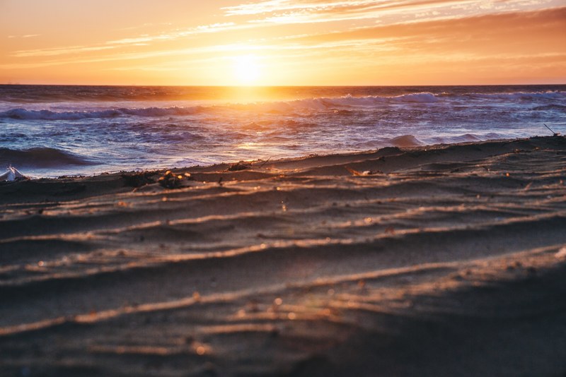 a sunset reflecting off the cresting waves over the horizon of a beach, sunset reflected in the seas waves 4k