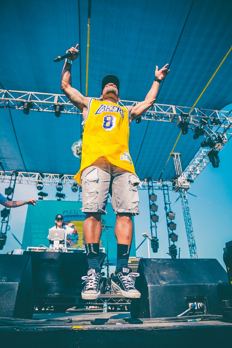 a man with a microphone in a yellow lakers shirt jumping up on stage, vocalist jumping on stage 4k