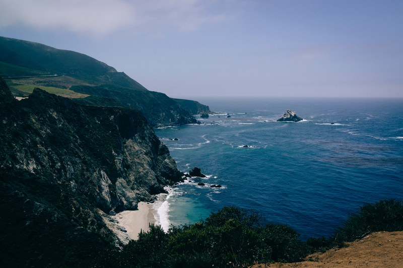 a dim shot of craggy hills over a deep blue sea, rocky coastline at big sur ca 4k