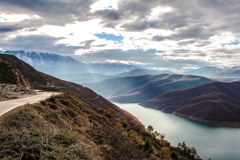 a scenic landscape with fjords and snowy mountains on the horizon, road along the fjord 4k