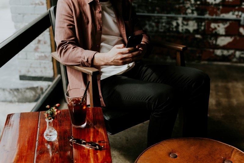 a male sitting at a table in a cafe holding a cellphone while enjoying a beverage, cafe texting 4k