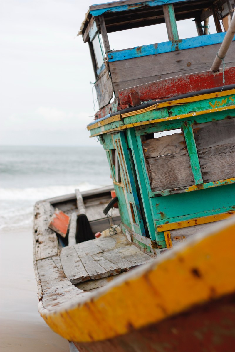 an old wooden boat painted in various colors on a sandy beach, get out 4k