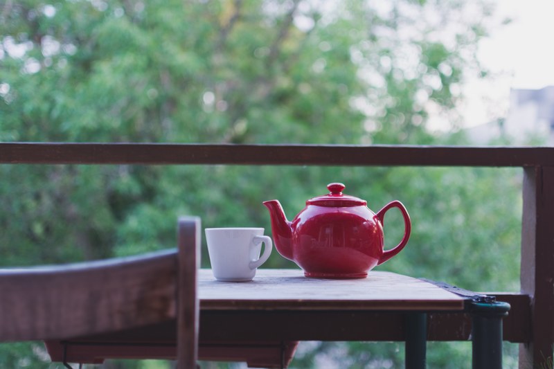 red teapot and white mug on an outdoor table with view of trees, teapot and mug on table 4k